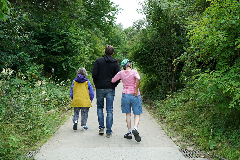 Das Bild zeigt drei Personen auf einem gemeinsamen Spaziergang im Grünen.