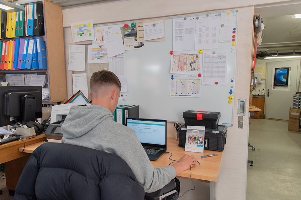 Das Bild zeigt einen jungen Mann in einer Werkstatt an einem Notebook arbeiten.