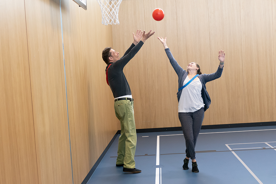 Das Bild zeigt einen Mann und eine Frau in einer Turnhalle unterhalb eines Basketballkorbes beim Ballsport.
