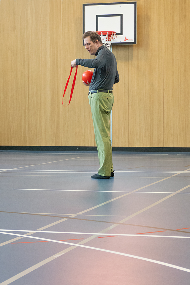 Das Bild zeigt einen Mann mit einem roten Ball und einem roten Markierungsband in der Hand.