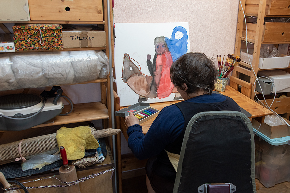 Das Bild zeigt eine Frau beim Kreidemalen in einem Atelier.