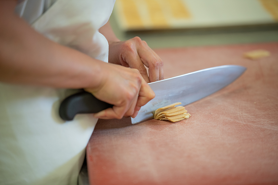 Das Bild zeigt eine Person die kleine Teigstücke mit einem grossen Küchenmesser in Portionen schneidet.