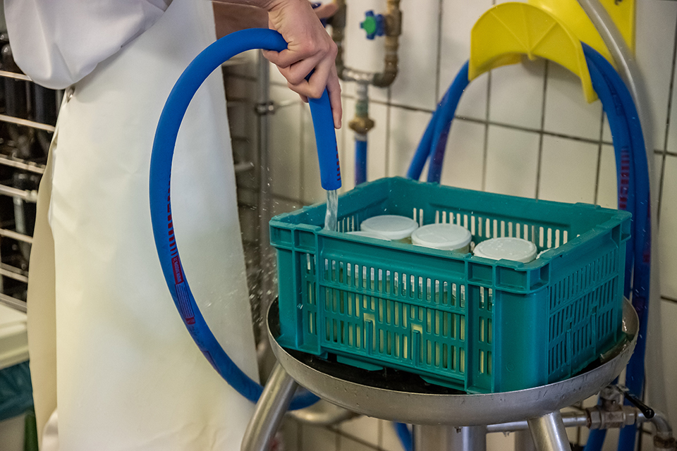 Das Bild zeigt eine Person die fertig abgefüllte Joghurtgläser mit Wasser, welches aus einem Schlauch kommt, reinigt.
