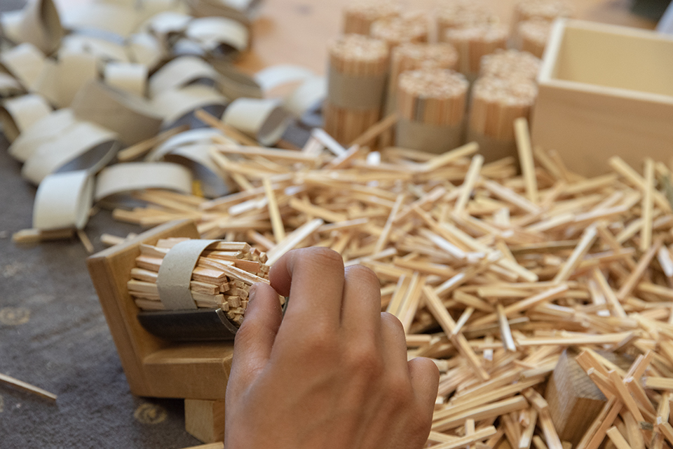 Das Bild zeigt eine Menge Holzstäbchen auf einem Tisch liegend. Die Holzstäbchen werden zu einem Bündel zusammengefügt und dienen als Anzündholz.
