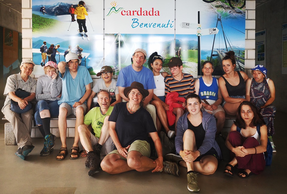 Das Bild zeigt eine grosse Menschengruppe sitzend vor einer Werbeblache des Ausflugsziels Cardada.