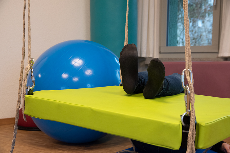 Das Bild zeigt eine grüne Schwebeliege und einen blauen Therapieball.