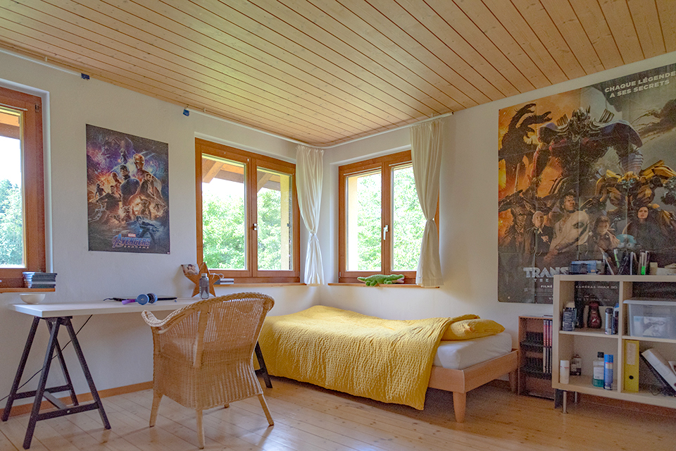Das Bild zeigt ein Schlafzimmer mit Bett, Schreitisch und Regal. An den Wänden hängen viele Filmposter.