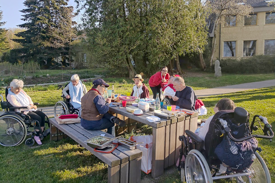 Das Bild zeigt eine Gruppe Menschen die an einem Tisch im Freien essen.