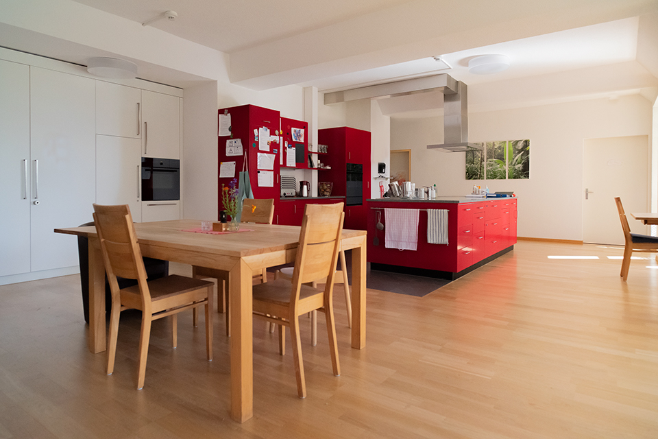 Das Bild zeigt eine rote Küchenzeile und einen kleinen Esstisch.