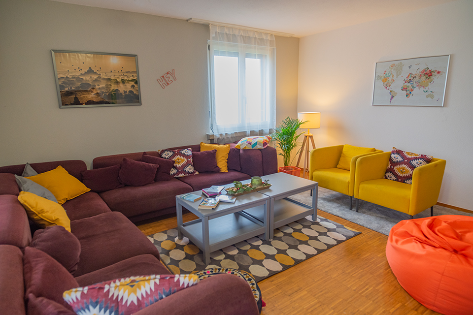 Das Bild zeigt ein Wohnzimmer mit auberginefarbenen und gelben Sesseln sowie einem orangen Sitzsack.