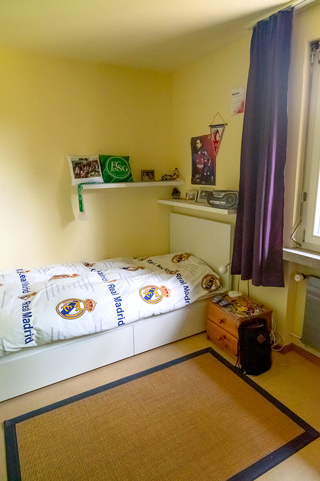Das Bild zeigt ein Schlafzimmer mit einem Bett und weissen Regalen an den Wänden.