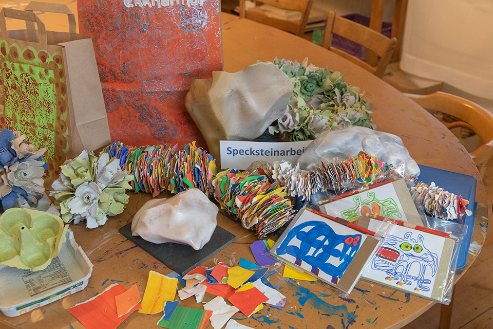 Das Bild zeigt einen Tisch auf dem viele verschiedene von Hand hergestellte Produkte ausgestellt sind. Zum Beispiel bemalte Papiertaschen, Schreibkarten und Weihnachtskugeln aus Eierkartons.
