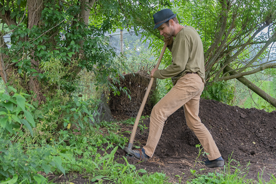Das Bild zeigt einen Mann beim Umgraben eines Komposthaufens.