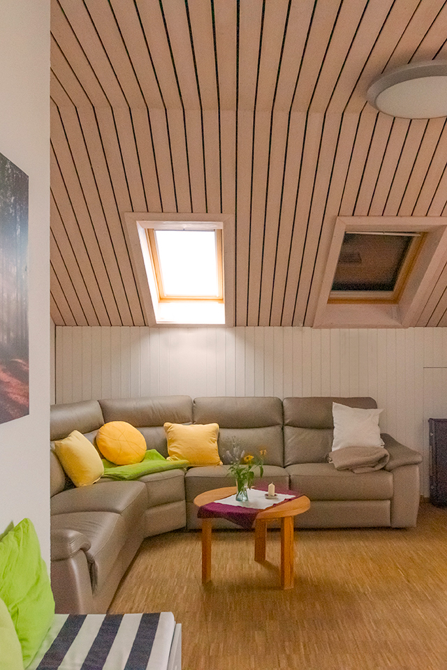 Das Bild zeigt ein Wohnzimmer mit graubraunem hellen Sofa und gelben und grünen Sofakissen.