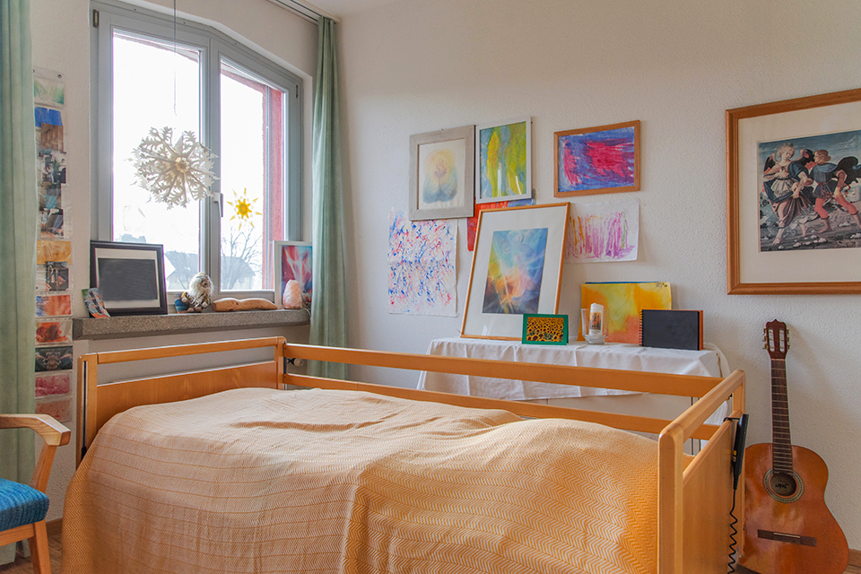 Das Bild zeigt ein Schlafzimmer mit Pflegebett und vielen Zeichnungen an den Wänden.