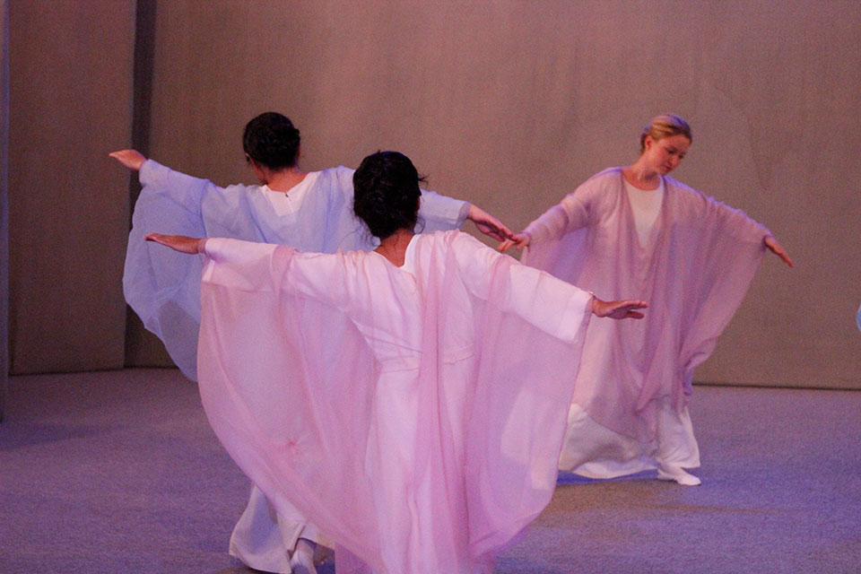 Das Bild zeigt drei Tänzerinnen in rosaroten Gewändern auf der Bühne.
