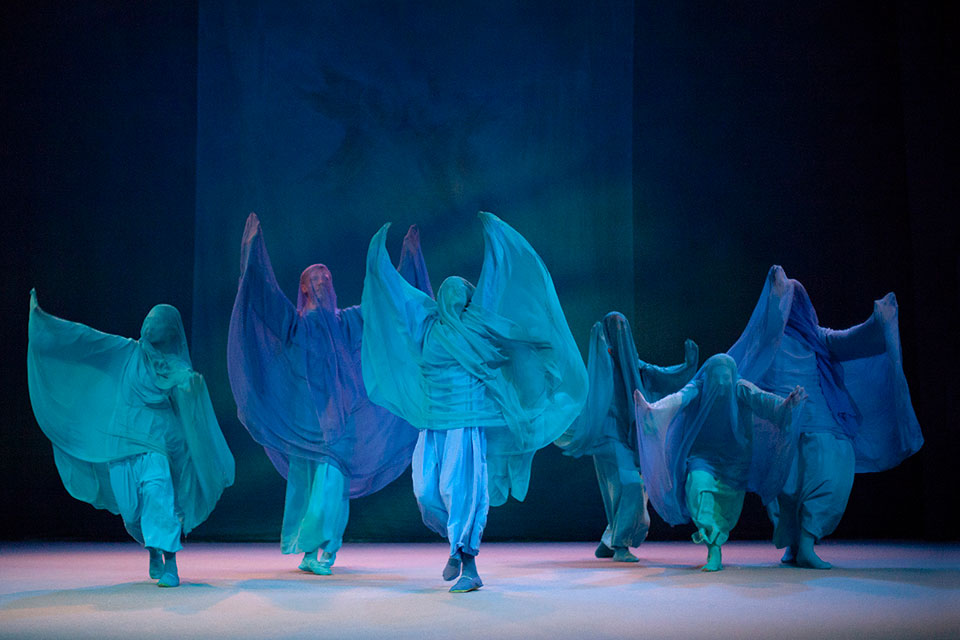 Das Bild zeigt sechs Tänzer in blauen Gewändern auf der Bühne.