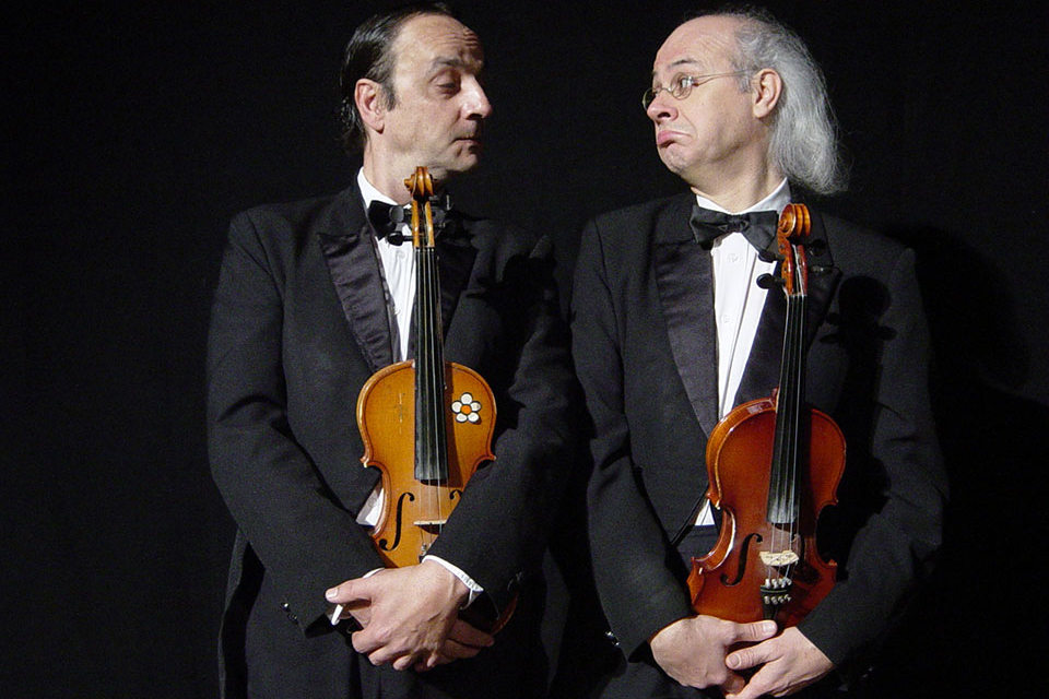 Das Bild zeigt zwei Männer mit Geige in der Hand auf der Bühne.