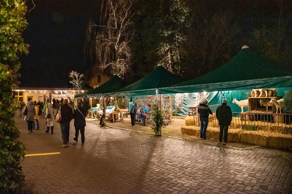 Das Bild zeigt Marktstände und Menschen am Abend auf einem Platz.
