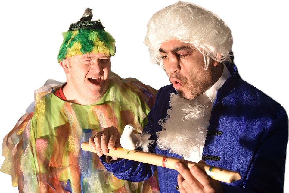 Das Bild zeigt zwei Männer. Der eine Mann als Mozart verkleidet mit einer Flöte und einem Vogel in der Hand. Der andere Mann trägt einen gelbgrünen Hut mit einem Vogel darauf.
