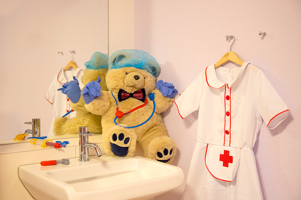 Das Bild zeigt einen als Arzt verkleideten Teddybären der auf einem Lavabo sitzt.