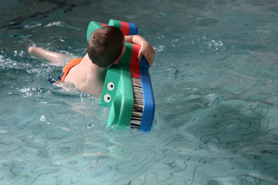 Das Bild zeigt einen Jungen der sich beim Schwimmen an einem Gummikrokodil festhält.