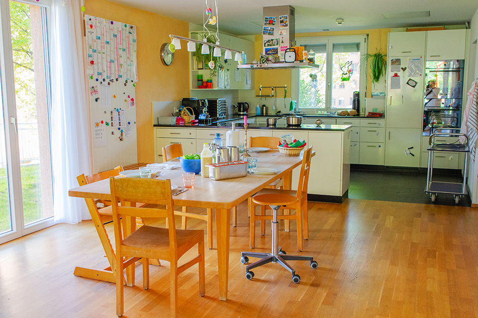 Das Bild zeigt ein weisse Küche und einen Esstisch aus Holz.