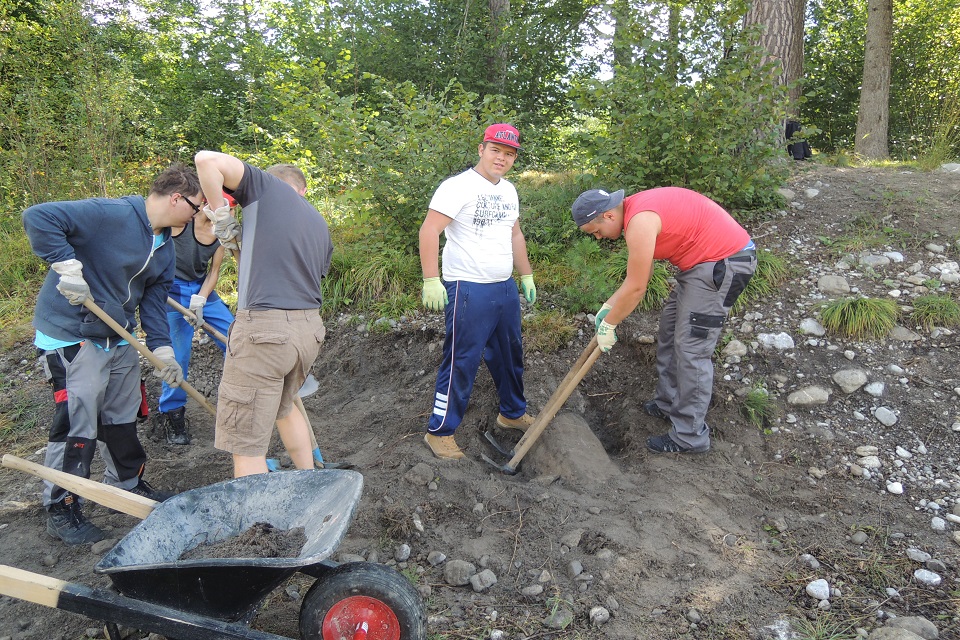Das Bild zeigt fünf Jugendliche mit Schaufeln und Spitzhacken die Steiner aus der Erde graben.