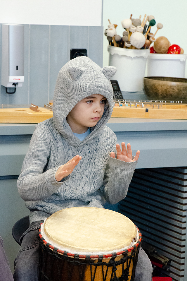 Das Bild zeigt einen Jungen der die Kapuze seines Pullovers über den Kopf trägt und am Trommeln ist.