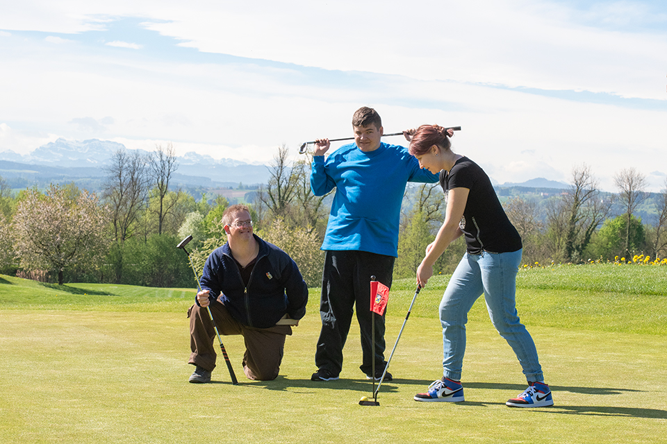 Das Bild zeigt zwei Männer und eine Frau auf einem Golf-Green.