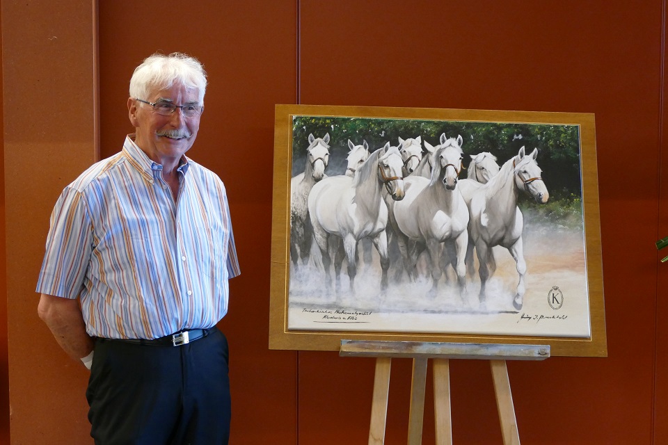 Das Bild zeigt Heinz Berchtold neben seinem Gemälde stehen. Das Gemälde zeigt acht weisse Pferde.