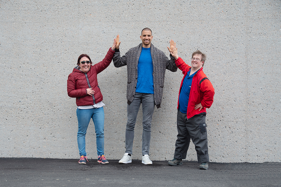 Das Bild zeigt drei Personen die vor einer Betonwand für ein Foto posieren.