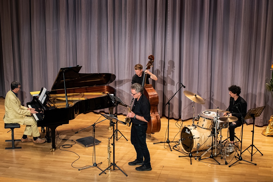 Das Bild zeigt einen Pianisten, einen Saxophonisten, einen Bassisten und einen Schlagzeuger auf der Bühne.
