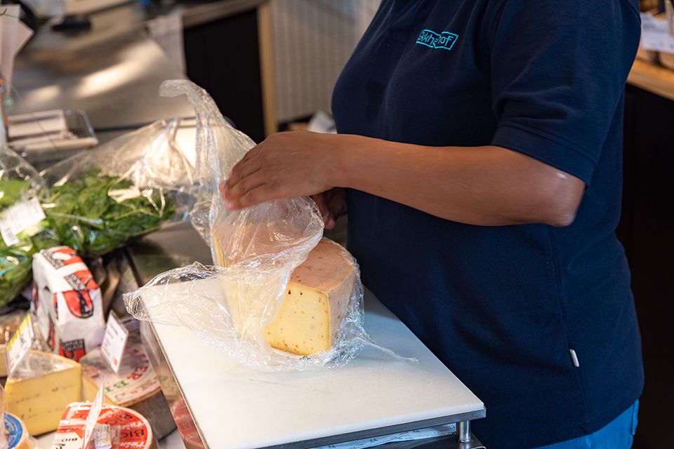 Das Bild zeigt eine Person beim Verpacken eines Käselaibes.