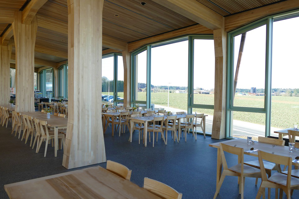 Das Bild zeigt einen grossen Speisesaal mit vielen Holztischen und Holzstühlen und einer grossen Fensterfront.