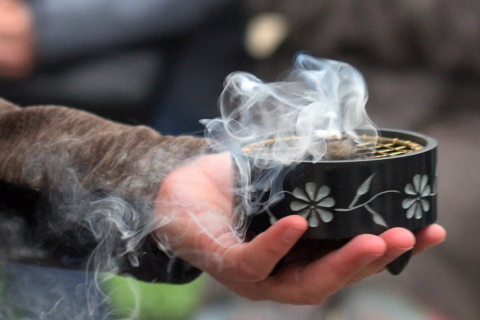 Das Bild zeigt eine Hand die einen Räuchertopf hält, aus dem Rauch aufsteigt.