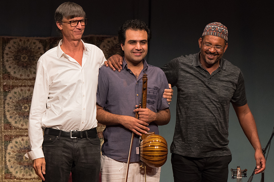 Das Bild zeigt drei Männer dem Publikum zugewandt auf der Bühne stehen.