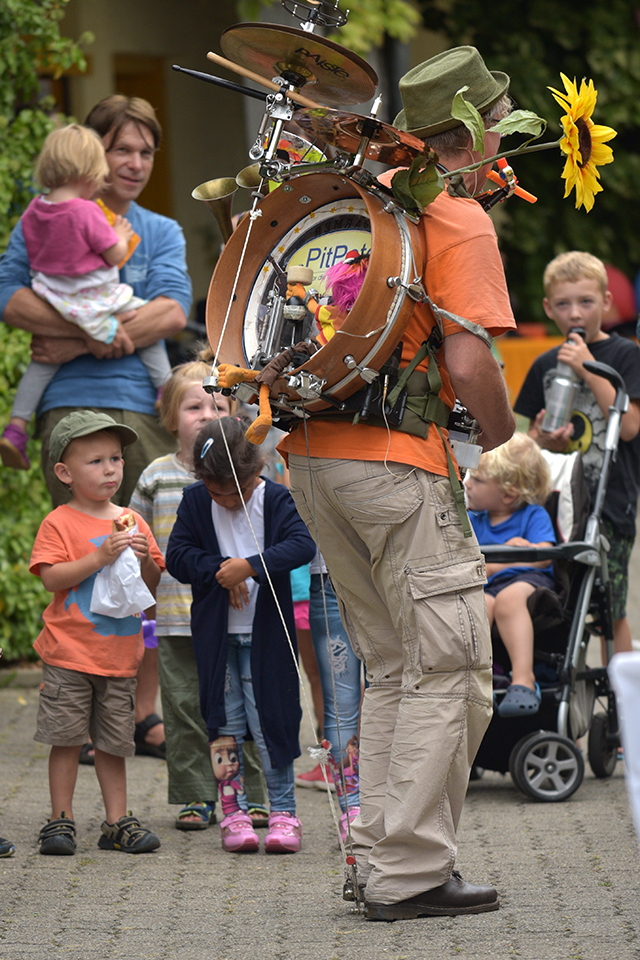 Das Bild zeigte einen Mann mit einer Trommel auf dem Rücken. Viele Kinder schauen dem Mann beim Musikzieren zu.