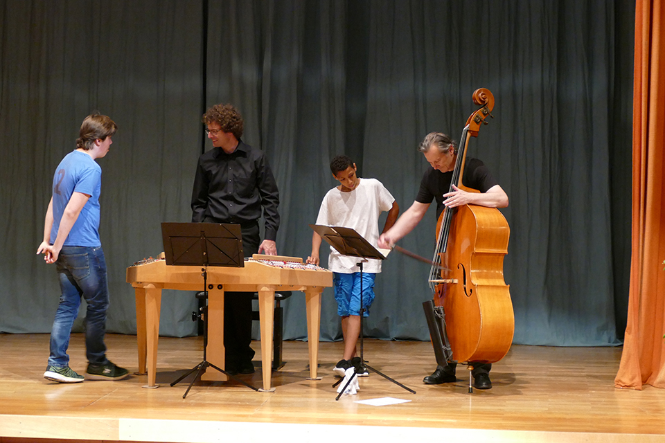 Das Bild zeigt Musiker die zwei Jugendlichen ihre Instrumente vorführen.