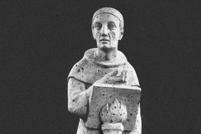 Zu sehen ist eine Steinfigur, vor der Figur ist ein Buch platziert aus Stein.