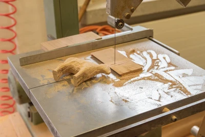 Auf der Arbeitsplatte einer Dekupiersäge liegt eine kleine Tierfigur aus Holz und viel Sägemehl.