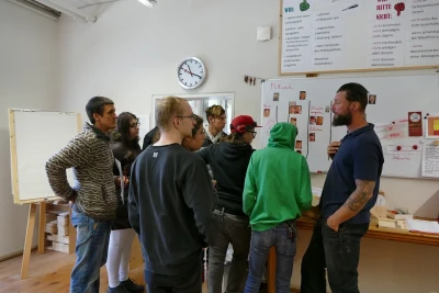 Zu sehen ist eine Grupper junger Menschen in einem Klassenraum. Dahinter ist eine beschriebene Tafel an der Wand angebracht.