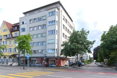 Man sieht ein grosses, mehrstöckiges Eckhaus in Kreuzlingen. Unten ist ein Laden, davor führt ein Zebrastreifen über die Strasse.