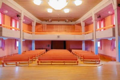 Zu sehen ist der Sitzbereich und die Tribüne des Veranstaltungssaals in orangen und roten Tönen.