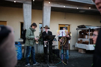 Zu sehen sind drei Blasmusiker mit ihren Instrumenten, die sich gerade bereit machen zum Spielen auf dem Weihnachtsmarkt.