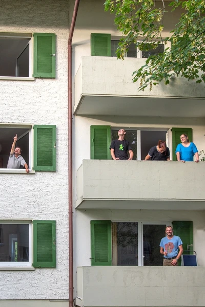 Zu sehen ist ein Ausschnitt einer Aussenansicht der Wohngruppe «Kleinfreiheit». Bewohner und Bewohnerinnen stehen auf dem Balkon.